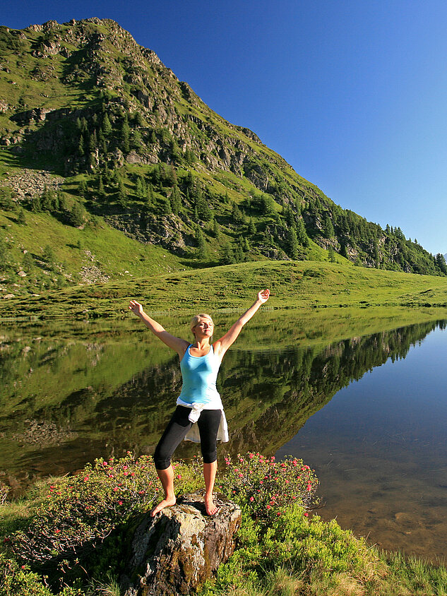 A woman enjoys nature at a mountain lake during her active vacation in Austria.