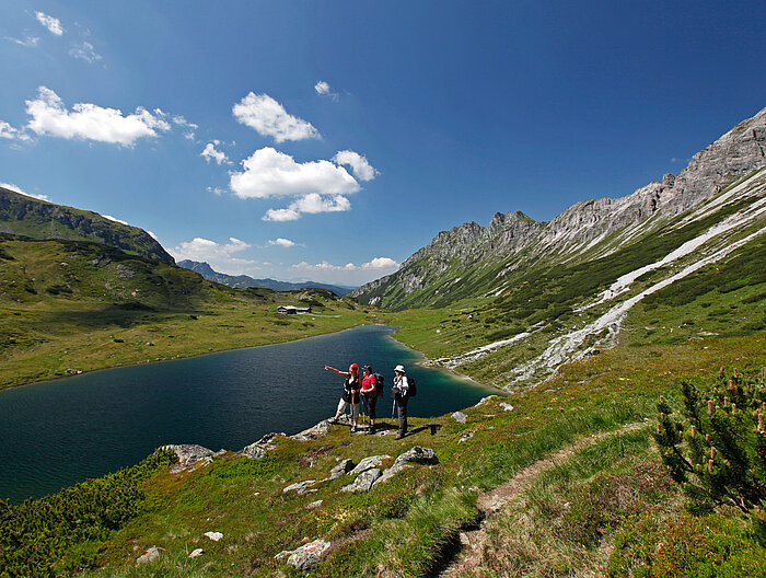 Three hikers enjoy the view of a mountain lake during an active vacation in Austria.