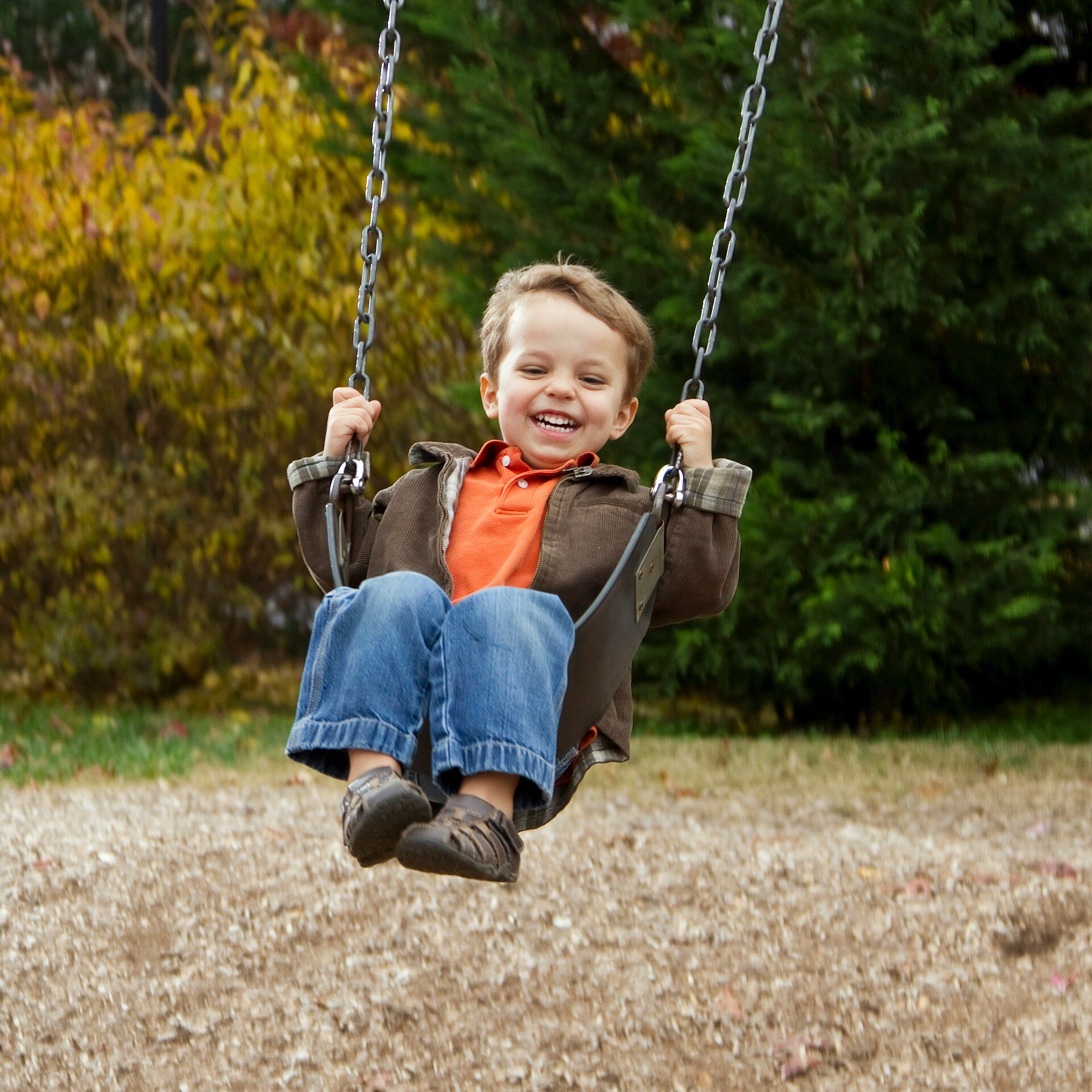 Boy laughing on a swing in a playground