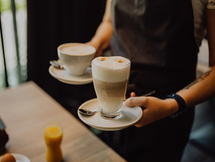 A member of staff carrying two cups of coffee at the Gourmet & Wellness Hotel Lürzerhof