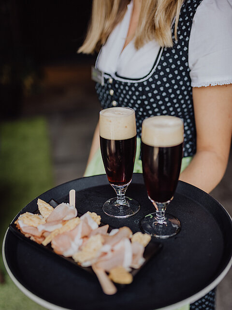 A member of staff with a tray containing a delicious snack and two drinks at the Gourmet & Wellness Hotel Lürzerhof.