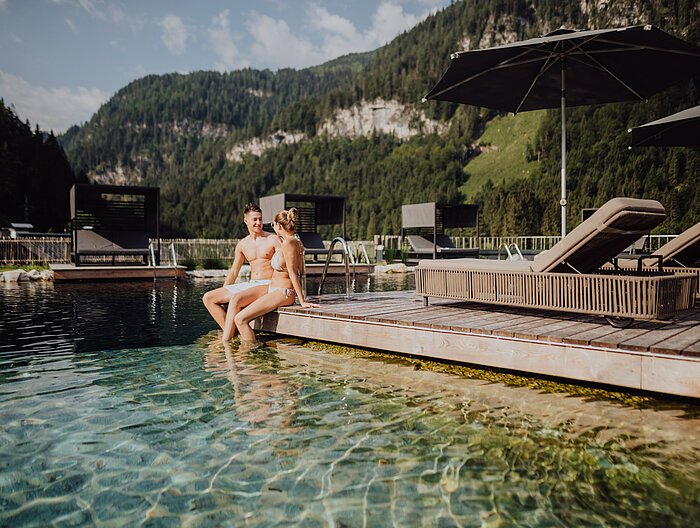 A couple relaxes on the jetty of the natural pool at the Lürzerhof wellness hotel in Salzburg.