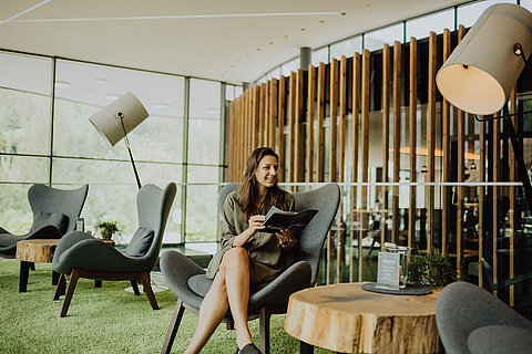 A woman relaxes in the lounge of the Lürzerhof and reads the bar menu.