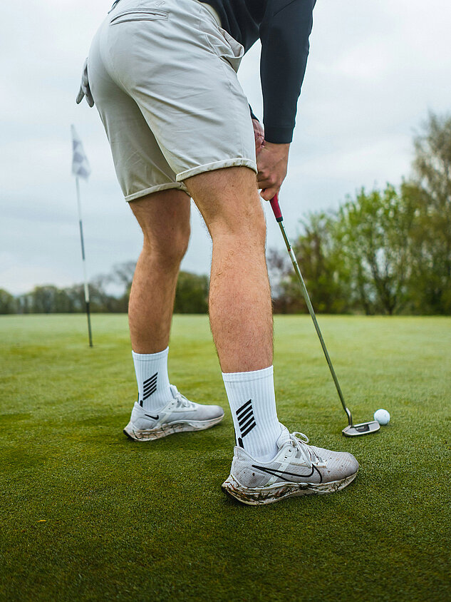 Golfer putting with ball in front of hole on green
