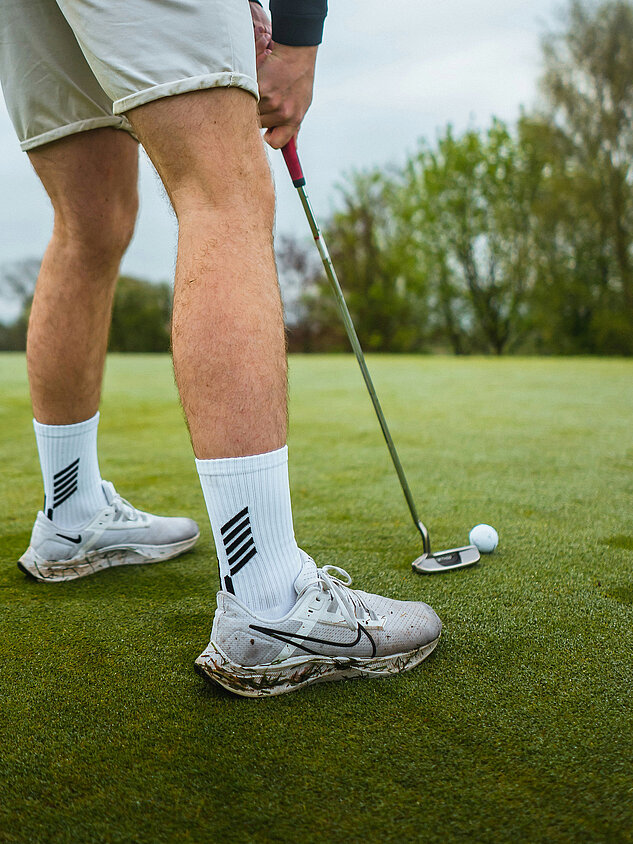 Golfer putting with ball in front of hole on green