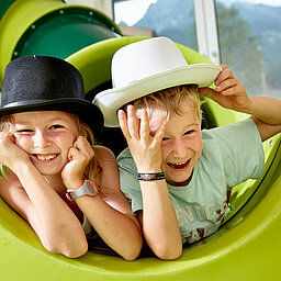 Two children play on a slide in the play area of the Lürzerhof, the family hotel in Austria for vacations with children.
