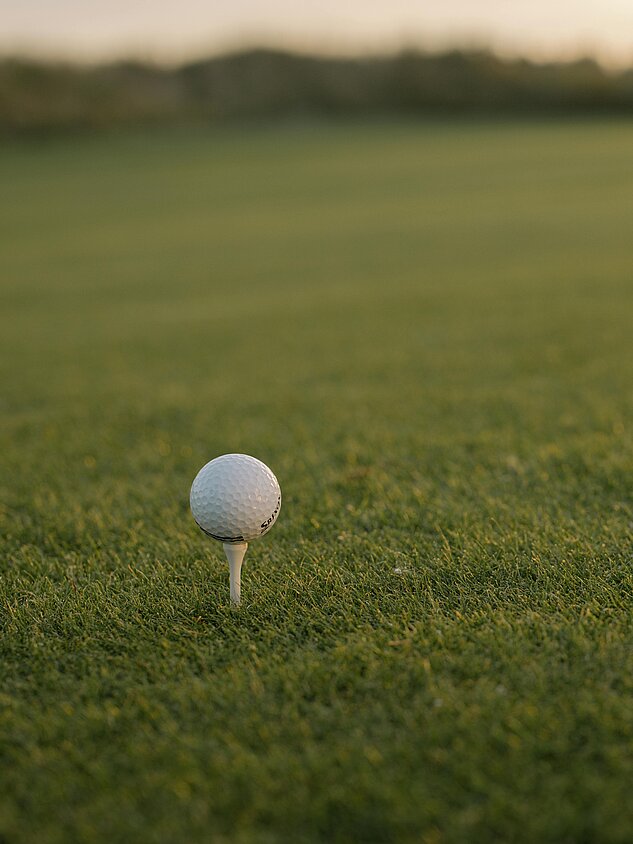 Golf ball on tee on well-kept green at sunset