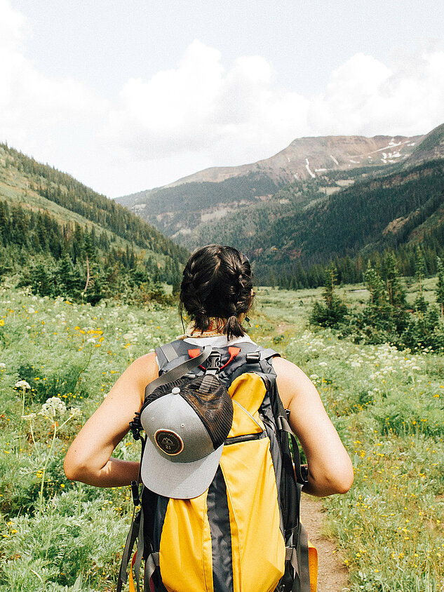 Woman with backpack hiking through a flower-filled valley in the mountains