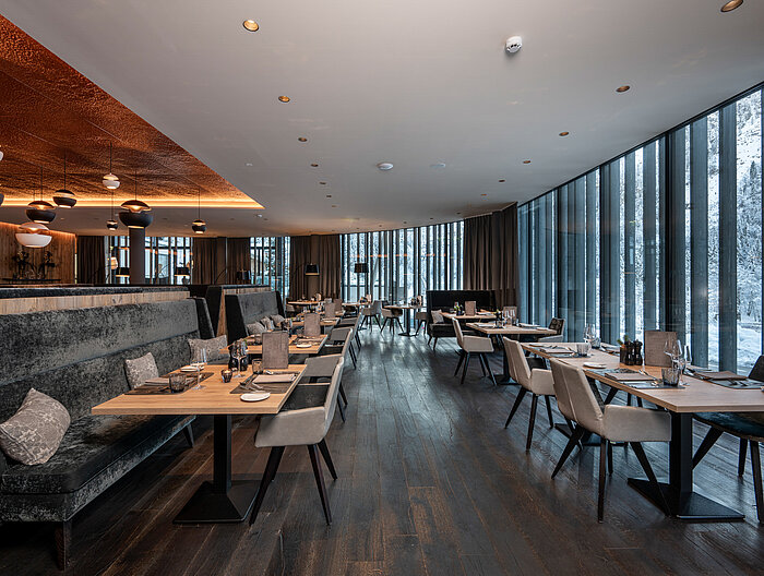 A stylishly decorated restaurant area in the Lürzerhof Gourmet & Wellness Hotel with panoramic views of the snow-covered mountain landscape.