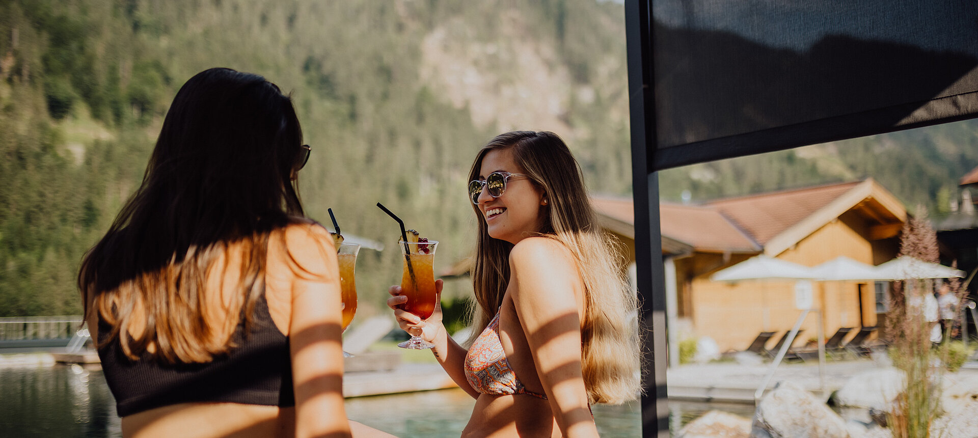 Two women enjoy the sun at the mountain lake pool at the Lürzerhof Wellness Hotel in Salzburg.
