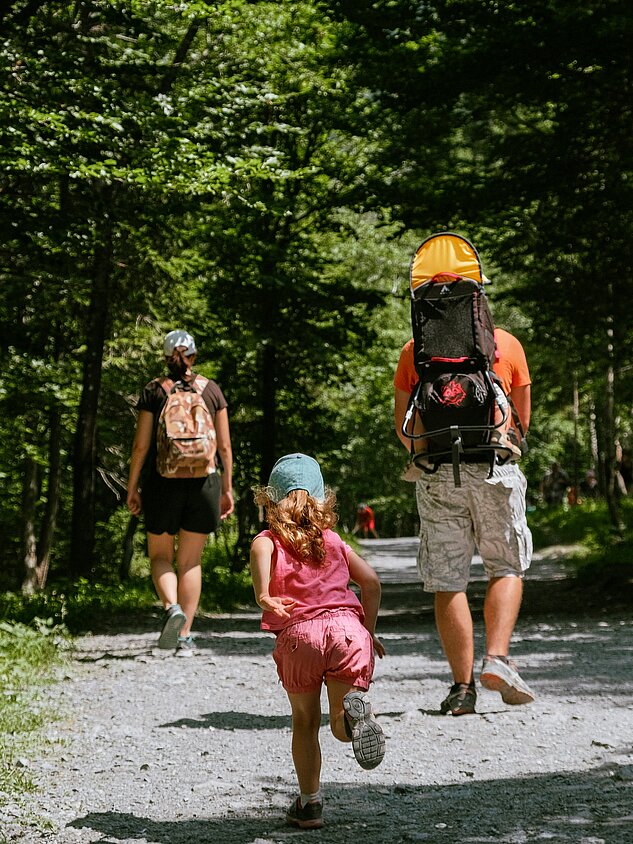 Sommerurlaub Familie wandert durch schattigen Waldweg mit Kleinkind