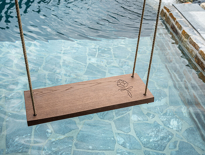 A wooden swing with an engraved logo above the natural pool at the Lürzerhof wellness hotel in Salzburg.