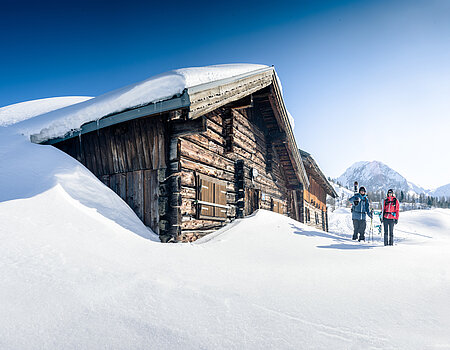 Two ski tourers in front of a snow-covered mountain hut in bright winter weather in Obertauern