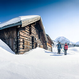 Two ski tourers in front of a snow-covered mountain hut in bright winter weather in Obertauern