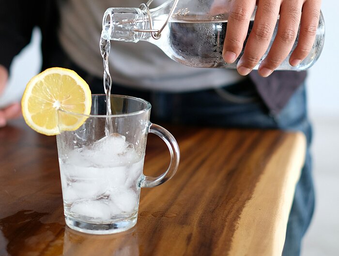 Man pours water from glass bottle into iced tea glass with lemon